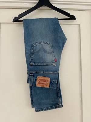 Levi's ljusblå slim straight jeans - Klassiska ljusblå jeans från Levi's med rak passform och femficksmodell. Jeansen har den ikoniska läderlappen bak i midjan och röd Levi's-tag på bakfickan. Tillverkade i slitstark denim, perfekta för en avslappnad och tidlös stil.