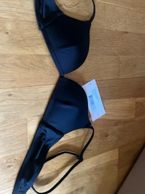 Svart bikiniöverdel från Nelly - Snygg svart bikiniöverdel från Nelly i modellen Illusions Bikini Bra. Enkel och stilren design med tunna axelband och slät yta. Perfekt för strandhäng eller poolen. Bikinin har en klassisk passform och är tillverkad i ett mjukt syntetmaterial.