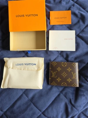 Louis Vuitton brun monogram plånbok - Snygg brun plånbok från Louis Vuitton i klassiskt monogrammönster. Tillverkad i canvas med insida i brunt läder och flera fack för kort och sedlar. Kommer med original ask, dustbag och certifikat. Perfekt accessoar för dig som gillar lyxiga detaljer.