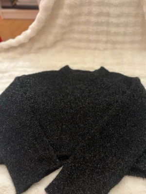 Svart glittrig stickad tröja H&M - Snygg svart stickad tröja från H&M med glittriga inslag som ger en festlig känsla. Tröjan har lång ärm och rund halsringning. Materialet är fluffigt och mjukt, perfekt för att hålla värmen under kyliga dagar.
