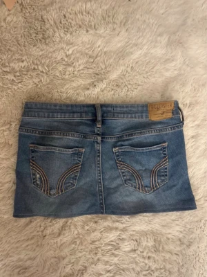 Blå jeanskjol från Hollister - Säljer en blå jeanskjol från Hollister med klassiska bakfickor och slitna detaljer framtill. Kjolen är i W24💓