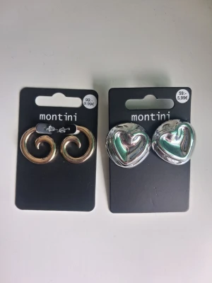 Två par örhängen från Montini guldfärgade/silverfärgade - Säljer två par örhängen från Montini. Ett par är guldiga med spiralformad design och ett par är silvriga med hjärtformad look. Båda paren är i metall och har en trendig, chunky stil som sticker ut.