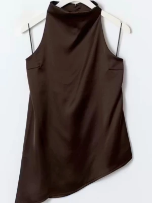 Asymmetrisk halterneck topp i satin - Snygg brun halterneck topp i glansigt satintyg med asymmetrisk nederkant och tunna axelband. Toppen har hög hals och öppen rygg. Toppen är i jättebra skick då den endast är använd en gång. Kontakta ifall du vill ha mer bilder på plagget:)