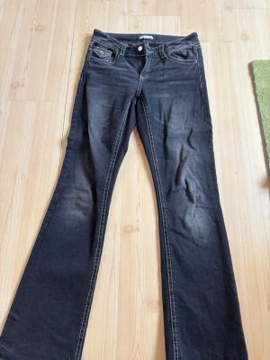 Svarta bootcut jeans med fickdetaljer - Säljer ett par svarta bootcut jeans med snygga kontrastsömmar. Jeansen har fram- och bakfickor med lock och knappdetaljer. Perfekta för dig som gillar en klassisk men trendig look.