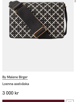 Svart axelväska By Malene Birger - Snygg svart axelväska från By Malene Birger med vitt grafiskt mönster och bred, justerbar axelrem. Väskan har guldfärgade detaljer och magnetlås. Insidan är beige och har flera fack för smart organisering. Perfekt för dig som vill ha både stil och funktion. Cirka 5 månader gammal