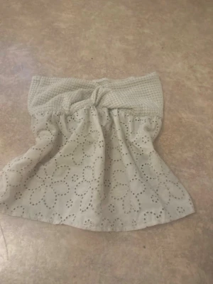 Vit tubtopp med broderade blommor - Söt vit tubtopp med bred ribbad kant upptill och broderade blommor över hela tyget. Toppen har en lätt utsvängd passform och är gjord i ett tunt, luftigt material som passar perfekt till sommaren.