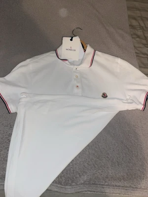 Vit Moncler pikétröja (nyskick) - Klassisk vit pikétröja från Moncler med korta ärmar. Storlek S passar M, nyskick med tagg medföljer.