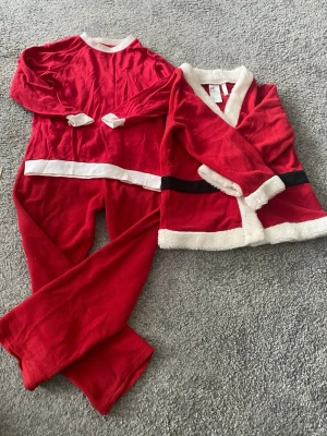Tomtedräkt barn H&M 122/128 - Röd tomtedräkt från H&M i mjuk fleece för barn, storlek 122/128. Setet består av byxor, tröja och jacka med vita och svarta detaljer samt fluffiga kanter. Perfekt till julens maskerad eller luciatåg!