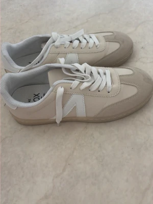 Beige och vita sneakers från VOX - Säljer nu mina snygga  sneakers från VOX i beige och vitt med vita snören och gummisula. Perfekta för en clean och stilren look.