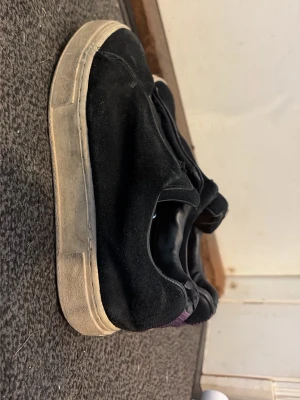Svarta sneakers med lila detalj - Svarta eytys sneakers i mockaliknande material med vit sula och lila tygdetalj på hälen. De är ganska slitna o väl använda. Kan sänka priset!
