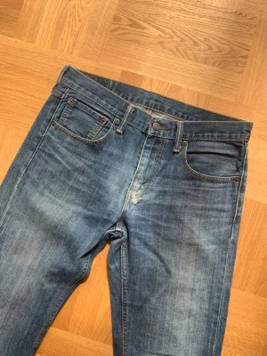 Levi's 527 Bootcut  - Snygga Levi’s jeans i bootcut-modellen 527 med en tydlig wash och fler aslitningar som höjer jeansen visuellt. Storlek 32 - utgå från angivna mått. Modellen är 178 cm lång och väger 65 kg.  Mått  Midja: 43	 Ytterben: 108 Innerben: 84 Benöppning: 23  Skriv vid frågor och funderingar!
