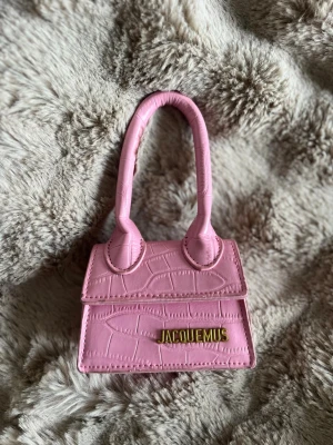 Rosa Jacquemus miniväska - Superfin miniväska i rosa från Jacquemus med krokodilpräglat mönster och guldfärgad logga framtill💓 Axelband följer med.