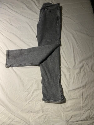 Grå raka jeans i klassisk modell - Tja. säljer ett par grå jeans med rak passform och fickor. Jeansen har en klassisk midja och vanlig tvättad look. Materialet är denim i bomull och de har en enkel, tidlös stil som passar till det mesta.