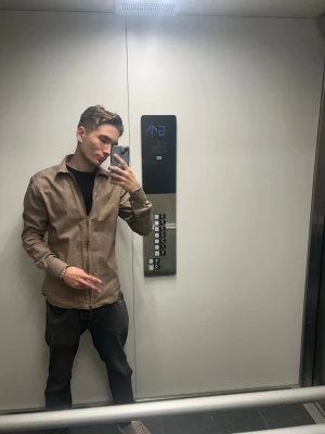 Beige John Henric skjorta med knappar - Säljer en stilren beige skjorta med knappar framtill och klassisk krage. Skjortan har lång ärm och en normal passform, perfekt för en clean och enkel look. Passar till både jeans och chinos.
