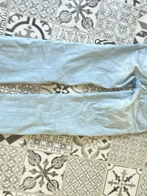 Ljusblå raka jeans med slitningar - Säljer ett par ljusblå jeans med raka ben och snygga slitningar framtill. Klassisk femficksmodell med dragkedja och knapp. Jeansen är gjorda i denim och har en avslappnad vibe som passar perfekt till vardagslooken. Midja:23 längd:32, med sprättade ner till.