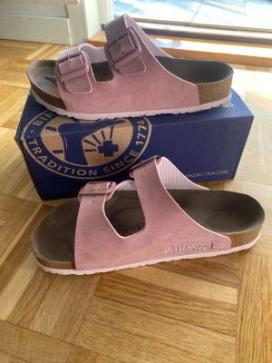 Rosa Birkenstock sandaler (Arizona) - Säljer ett par rosa Birkenstock sandaler i mocka, otroligt sköna och snygga, helt oanvända (sko boxen får du med vid köp)🩷🙌🏻