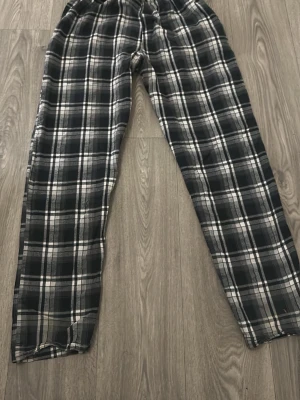 Rutiga pyjamasbyxor i svart och vitt - Mysiga pyjamasbyxor med svartvitt rutmönster och elastisk midja. Tillverkade i mjukt tyg som passar perfekt för hemmakvällar eller lata morgnar. Klassisk rak passform och tidlös design som funkar året runt.