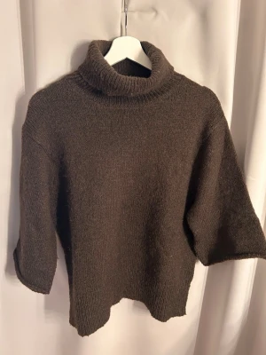 Brun polotröja från NA-KD - Mysig brun stickad polotröja från NA-KD med bred polokrage och trekvartsärmar. Tröjan har en avslappnad passform och är perfekt för kyliga dagar. Materialet är mjukt och ger en skön känsla. Enkel att matcha med jeans eller kjol.