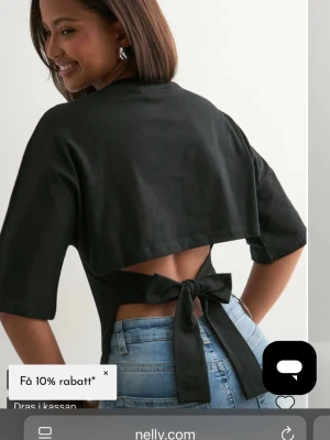 Svart croppad topp med knyt i ryggen - Snygg svart croppad topp med öppen rygg och breda knytband bak. Toppen har korta ärmar och en stilren, minimalistisk look som passar perfekt till jeans eller kjol. Lite nopprig vilket syns på bilden