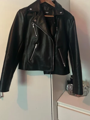 Svart skinnjacka från Bik Bok - Snygg svart skinnjacka från Bik Bok. Med silvriga dragkedjor. Jackan har flera fickor med dragkedja. Aldrig använd så som ny!