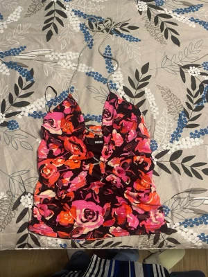 Blommig halterneck topp från Bik Bok - Snygg blommig halterneck topp från Bik Bok i starka färger som rosa, orange och röd på svart botten. Toppen har tunna knytband i nacken och en croppad passform. Perfekt för dig som vill sticka ut med ett färgstarkt plagg!