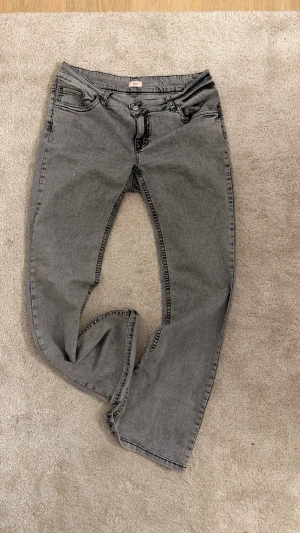 Grå bootcut jeans med broderade fickor - Säljer ett par grå jeans med rak passform och klassisk femficksdesign. Jeansen har normal lite låg midja.