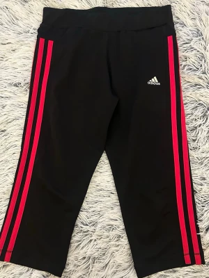  Adidas capri leggings med rosa ränder - Svarta leggings från Adidas med rosa ränder och Adidas-logga på låret. Tillverkade i ett stretchigt material som passar perfekt till träning eller chill. Storlek 11/12 år? 💖