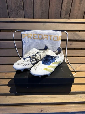 Vita Adidas Predator fotbollsskor 45 1/3 - Säljer ett par vita Adidas Predator fotbollsskor med guldiga detaljer. Skorna är i storlek 45 1/3 men passar 45. Skorna är i bra skick och använda få ggr men har blivit lite smutsiga då de är vita men går att tvätta bort. Dobbarna är i bra skick då de är sparsamt använda. Hör av er vid frågor!