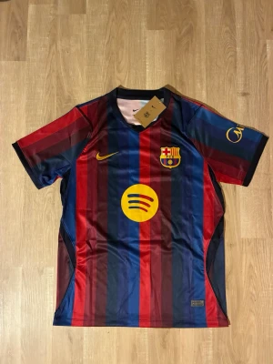 FC Barcelona Hemmatröja 26/27 Lamine Yamal - Säljer en FC Barcelona Hemmatröja för den aktiva säsongen 26/27 med Lamine Yamal och nummer 10 på ryggen. Tröjan har klassiska blå och röda vertikala ränder, klubbmärke och sponsorloggor i gult. Tillverkad i lätt och ventilerande funktionsmaterial. HELT NY!