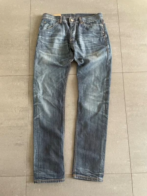 Dondup jeans - Säljer ett par blå jeans med raka ben. Jeansen har klassisk femficksdesign, knappgylf och kontrastsömmar. Materialet är denim och färgen är tvättad blå med ljusare partier. 