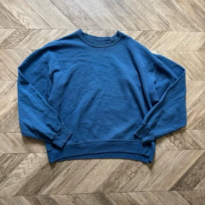 Blå sweatshirt från Fruit of the Loom - Klassisk blå sweatshirt från Fruit of the Loom med rund halsringning och ribbade muddar vid ärmslut och nederkant. Tillverkad i mjukt material som känns skönt mot huden. Perfekt för en avslappnad och stilren look.