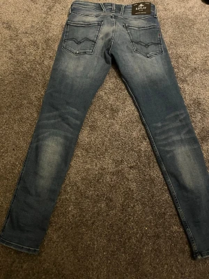 Blå slim fit jeans från Replay - Snygga blå slim fit jeans från Replay med klassisk femficksdesign och diskreta slitningar på framsidan och baksidan. Jeansen har normal midja och raka ben. Materialet är mjukt denim som ger en bekväm känsla och cool look.