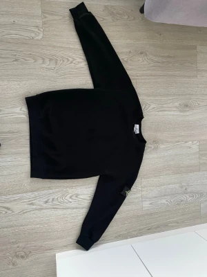 Svart sweatshirt med patch på ärmen - En stilren svart sweatshirt med rund hals och ribbade muddar. Tröjan har en patch på vänster ärm som ger en cool detalj. Perfekt till jeans eller joggers för en avslappnad look.