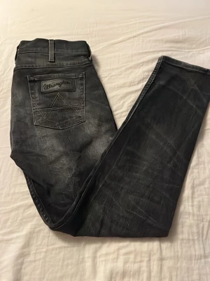 Svarta jeans från Wrangler - Snygga svarta jeans från Wrangler med slitna detaljer och klassisk femficksmodell. Jeansen har raka ben och tydliga sömmar på bakfickorna med Wrangler-logga. Perfekta för en avslappnad och cool stil.