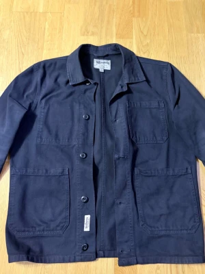 Marinblå overshirt/ Jacka - Stilren svart overshirt med tre stora utanpåliggande fickor och knäppning framtill. Tillverkad i kraftig bomullscanvas som ger en robust känsla. Klassisk krage och raka ärmar, perfekt för lager-på-lager-stil. Men kan även användas som en overshirt.  