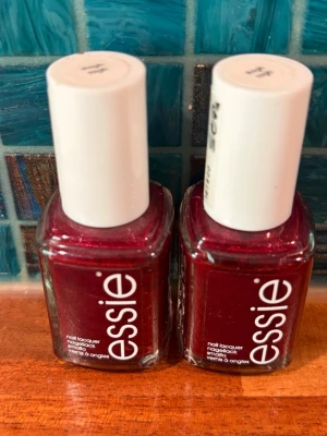 Essie-nagellack - Två flaskor Essie nagellack i ”Thigh High”, en djup mörkröd nyans med subtilt skimmer. Klassisk fyrkantig glasflaska med vit kork och tydlig logga. Perfekt för dig som vill ha snygga, glansiga naglar med en elegant touch. Den ena är ny och den andra testad en gg. 