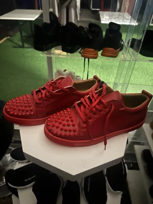 Röda sneakers med nitar - Unika helröda christian louboutin sneakers med nitar över hela tån och sidan. Skorna har lågt skaft, matchande röda skosnören och en tjock röd sula. Materialet ser ut att vara en mix av läder och mocka för en cool och edgy look.