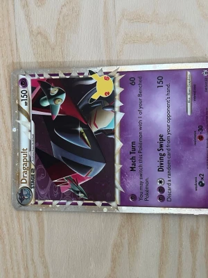 Pokémonkort Dragapult holo - Säljer ett Pokémonkort med Dragapult-motiv. Kortet har en holo-effekt och lila bakgrund med guldkant. Det är en Stage 2-kort med 150 HP och attacker som Mach Turn och Diving Swipe. Perfekt för samlare eller Pokémonfans!