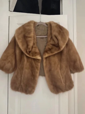 Kort brun pälscape med stor krage - Säljer en snygg kort pälscape i ljusbrun färg med stor krage och trekvartsärmar. Capen har en klassisk vintage-look och är fodrad på insidan. Perfekt för dig som vill ha en statement piece till vintern.