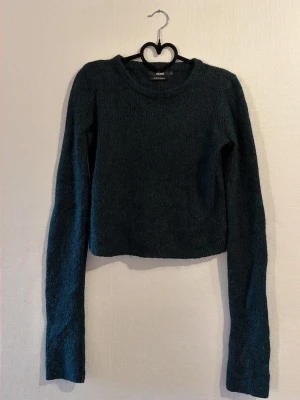 Mörkgrön croppad stickad tröja - Mysig mörkgrön stickad tröja med croppad passform och långa ärmar. Tröjan har rund halsringning och är tillverkad i mohair blandning. 
