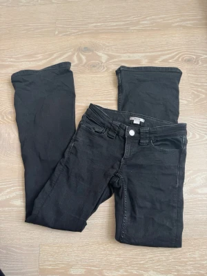 Svarta bootcut jeans med låg midja - Säljer ett par svarta bootcut jeans med låg midja och klassisk femficksmodell. Jeansen har en snygg passform som sitter tight över låren och släpper ut vid vaden. Perfekta till sneakers eller boots och passar till många olika stilar.