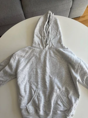 Ljusgrå hoodie med magficka - En basic ljusgrå hoodie med huva och dragsko. Hoodien har en stor magficka framtill och ribbade muddar vid ärmslut och nederkant. Perfekt för en avslappnad och chill stil. Materialet känns mjukt och bekvämt.