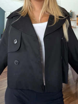 Svart trenchcoat med knappar - Säljer denna superfina stilrena korta trenchcoat med stora knappar framtill. 