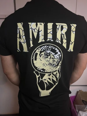 AMIRI svart T-shirt med färgglatt tryck - Svart T-shirt med snyggt AMIRI-tryck fram och stort motiv på ryggen. Stilren design med färgglada detaljer. I fint skick och bekväm passform. Perfekt till en streetwear-look.