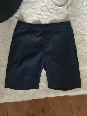 Mörkblå shorts från Adidas golf  - Snygga mörkblå shorts från Adidas med klassisk passform och diskret logga på bakfickan. Shortsen har bälteshällor och en bakficka, perfekta för en clean och sportig look. Materialet känns lätt och smidigt, vilket gör dem sköna att bära under varma dagar.