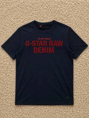 Marinblå G-Star Raw t-shirt - Snygg marinblå t-shirt från G-Star Raw med röd text 'G-STAR RAW DENIM' på bröstet. Klassisk passform med korta ärmar och rund halsringning. Perfekt till jeans eller shorts för en avslappnad look.