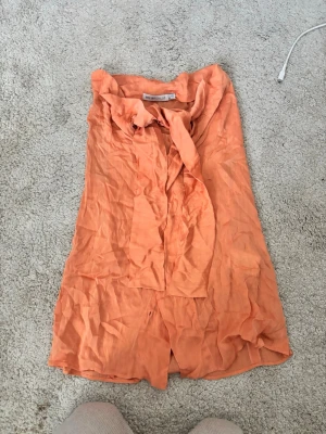 Persikofärgad blus med knytband  - Säljer en persikofärgad blus från i storlek L. Passar mig som S! Blusen har ett dekorativt knytband vid halsen och är tillverkad i ett lätt, tunt tyg. Perfekt till både vardag och fest! Blusen är använd men i fint skick, dock något skrynklig på bilden. Säljes pga garderobsrensning.