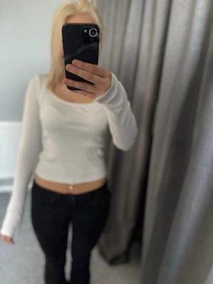 Vit ribbad långärmad topp H&M - Säljer en vit ribbad långärmad topp från H&M. Modellen är croppad med figurnära passform och har en rundad halsringning. Perfekt att styla med höga jeans eller kjol för en clean look.