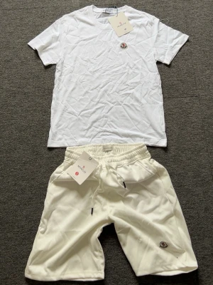 Vitt set från Moncler med t-shirt och shorts - Säljer ett fräscht vitt set från Moncler med en klassisk t-shirt och matchande shorts. Båda plaggen har Moncler-logga framtill och är gjorda i mjukt bomullsmaterial. Perfekt för en clean och avslappnad look.