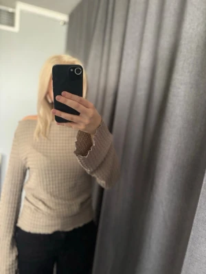 Beige off shoulder tröja - Trendig beige off shoulder tröja med rutigt mönster och vida ärmar. Tröjan har vågiga kanter vid ärmsluten och en avslappnad passform som ger en cool och modern look.